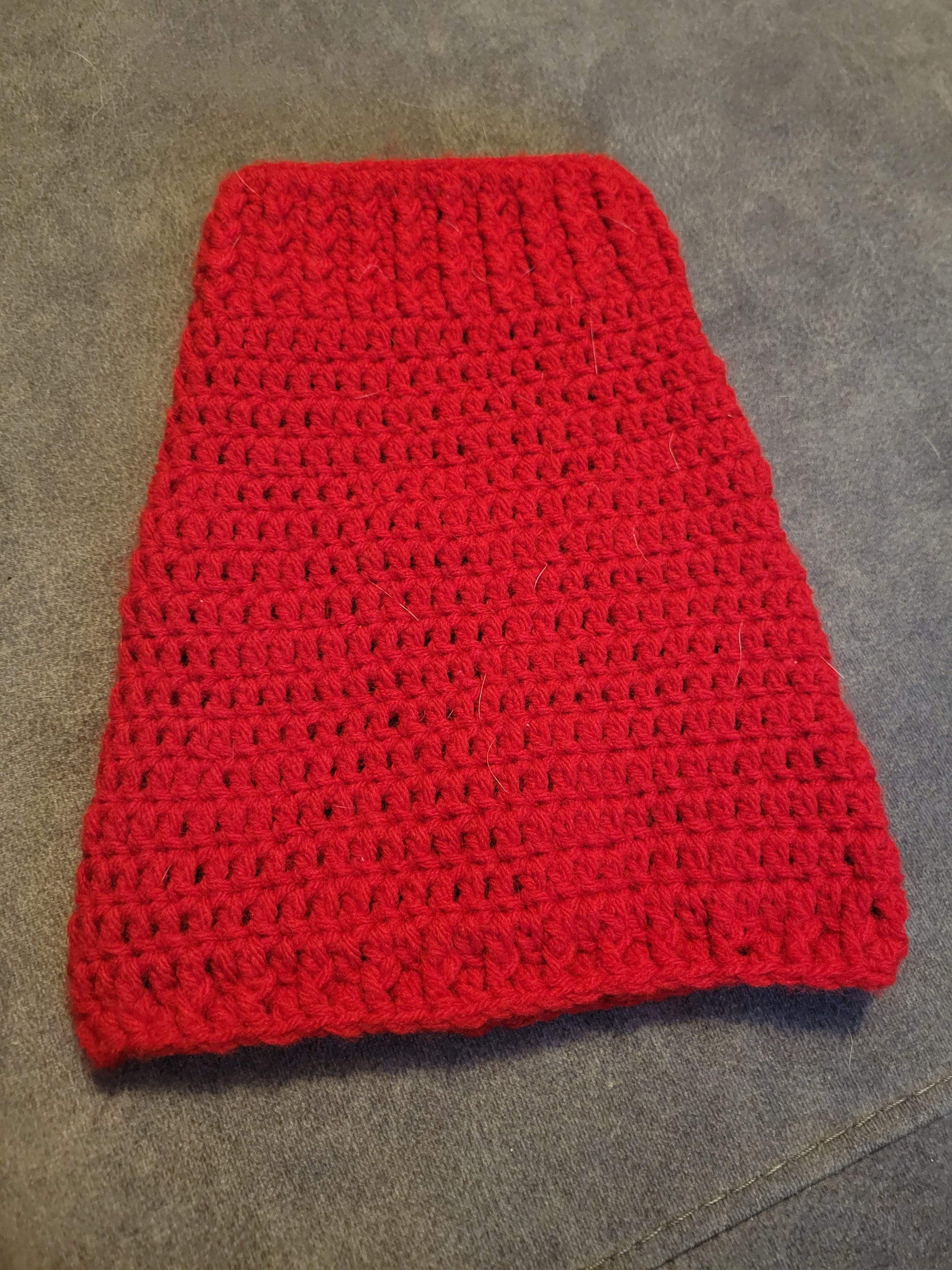 Red crocheted puppy sweater on gray surface